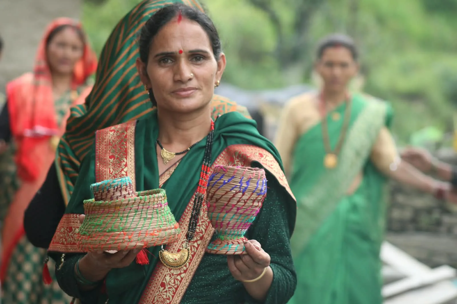 A woman in a green sari holds up two woven baskets