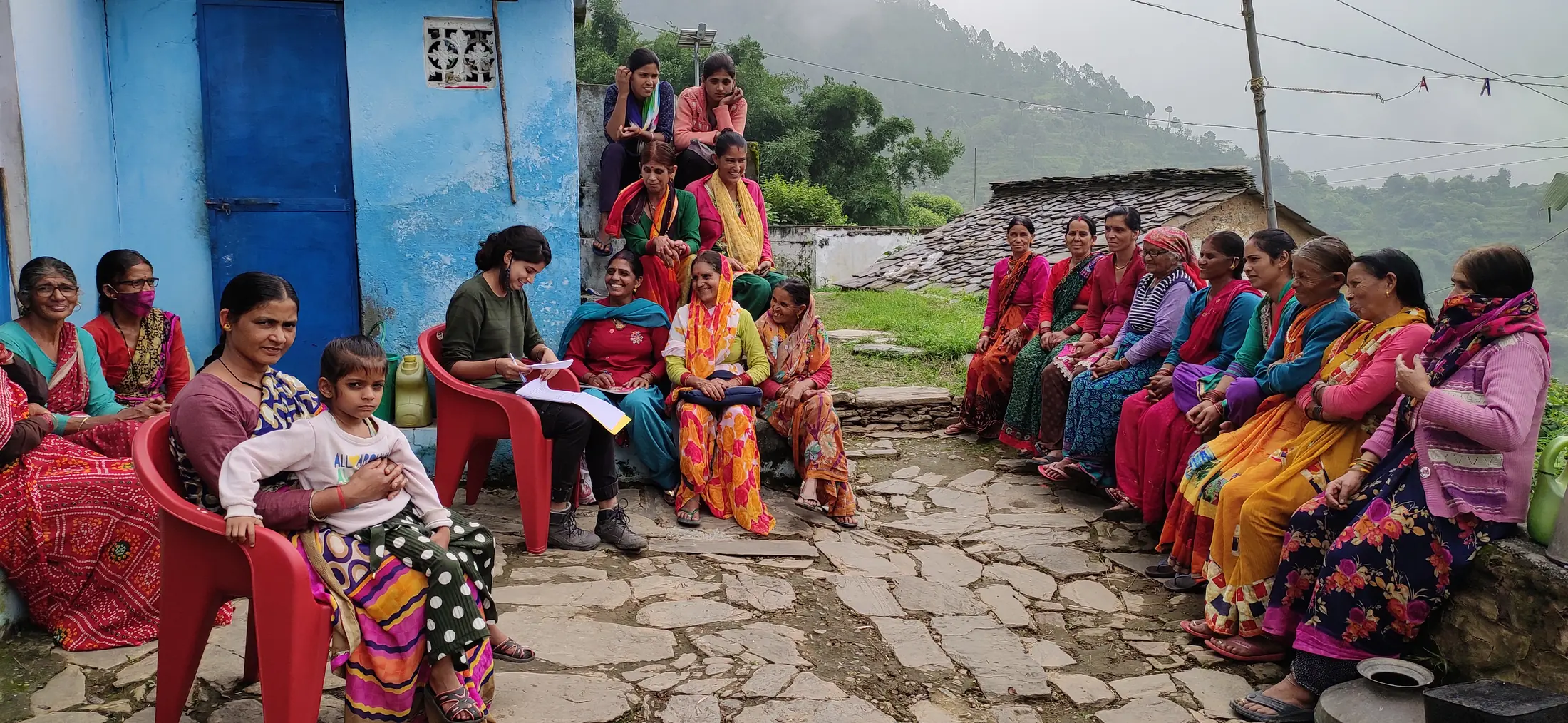 Village women meet in a circle outside a blue house in the hills