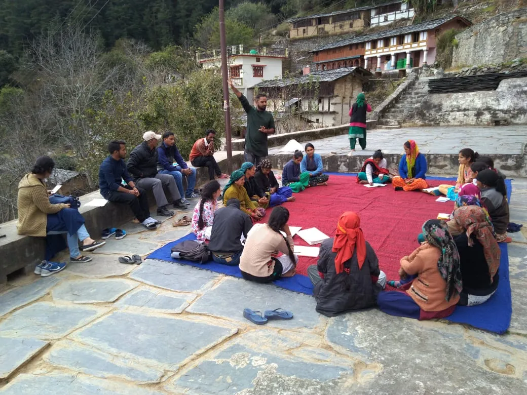 Villagers meet in a courtyard around a map drawn on the floor to plan work in their village