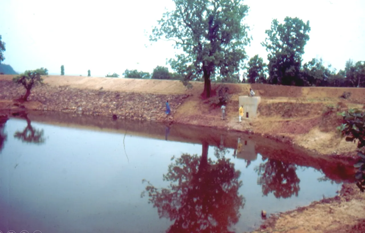 An earthen dam holding a pond of water in a dry landscape