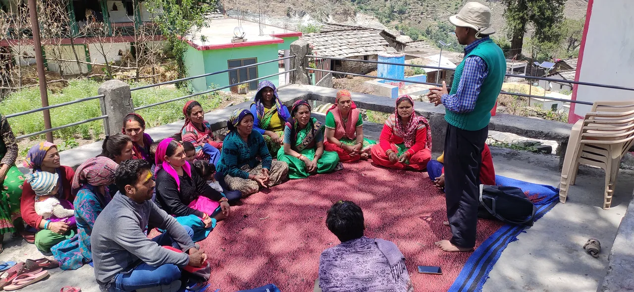 Village women and men sit in a circle for a community meeting